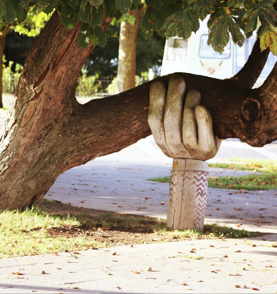 Baum der durch große geschnitzte Hand aus Holz abgestützt wird