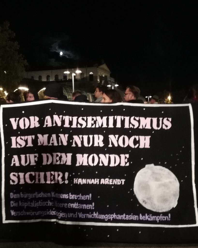 Ein Banner wird von mehreren Menschen bei der Mahnwache in Hannover am 10.10.2019, einen Tag nach dem antisemitischen Anschlag in Halle getragen. Darauf steht: "Vor Antisemitismus ist man nur noch auf dem Monde sicher", Hannah Arendt. Im Hintergrund sind die Straßenlaterenen an, es ist dunkel, vermutlich Abend.