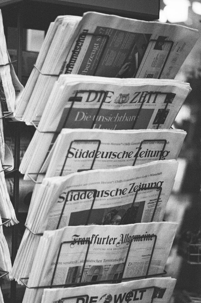 Schwarz-Weiß-Foto eines Kiosk-Zeitungsständers. Die Titelblätter von "Die Zeit", "Süddeutsche Zeitung" und Frankfurter Allgemeine" sind zu erkennen
